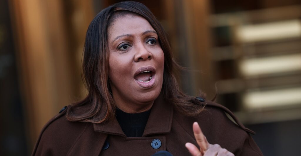 Letitia James makes a point while standing at a podium during a press conference and holds her left hand out.