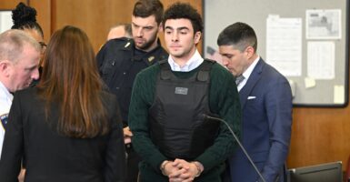 Luigi Mangione stands in a courtroom wearing a bulletproof vest with his hands folded in front of him.