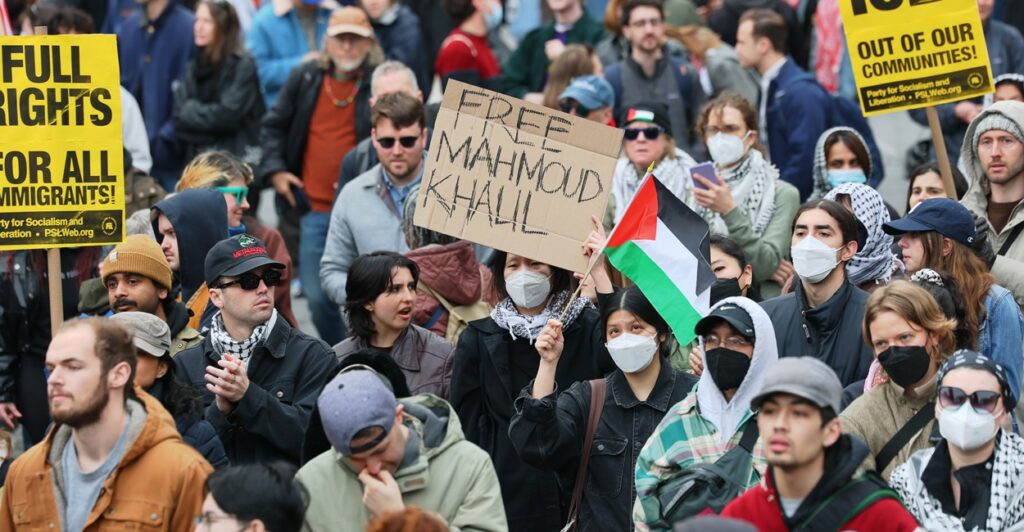 A person surrounded by protesters holds up a handmade sign that says "Free Mahmoud Khalil"