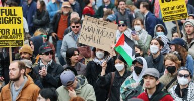 A person surrounded by protesters holds up a handmade sign that says "Free Mahmoud Khalil"