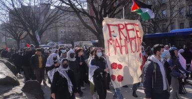 Several protesters walk down a street carrying a sign that says, "Free Mahmoud".