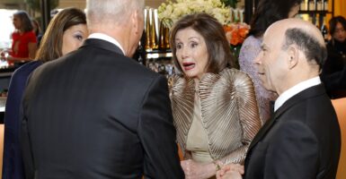 Nancy Pelosi talks with guests who are formed in a circle around her at a party.