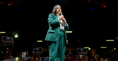 Rochelle Garza holding a microphone while standing on stage wearing a green blazer.