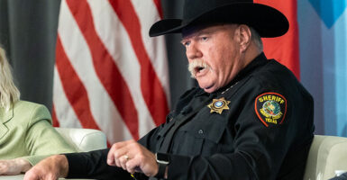 Sheriff Bill Waybourn wears a black cowboy hat and uniform while sitting in front of an American flag.