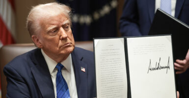 President Donald Trump in a suit with a blue tie holds up an executive order he signed.