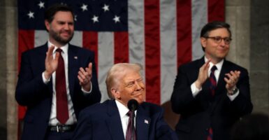 Donald Trump stands at a podium and smiles as he looks out onto the crowd.