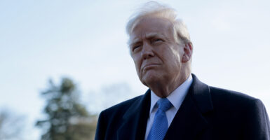 Donald Trump in a black suit with a blue tie looks bemused outside