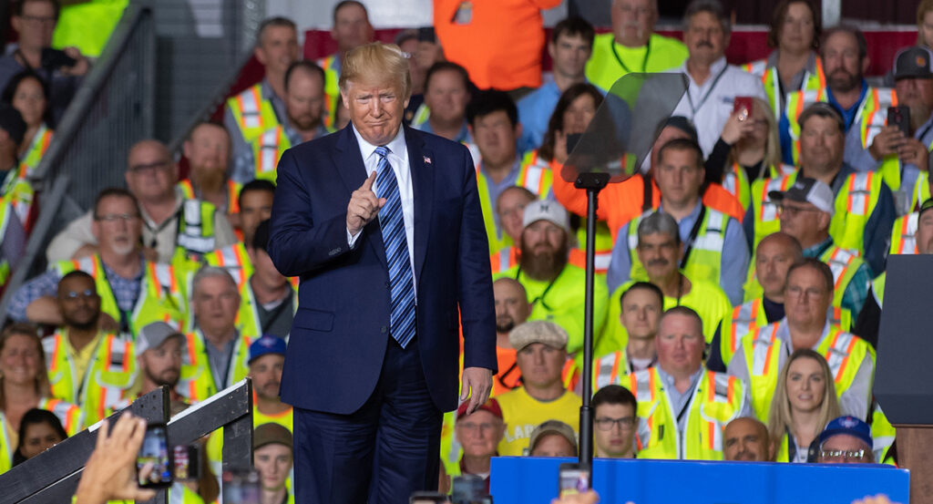 Donald Trump in a blue suit gestures in front of Shell workers