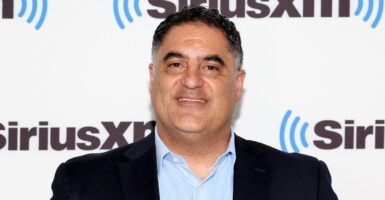 Cenk Uygur stands on a red carpet during an event and smiles at the camera.