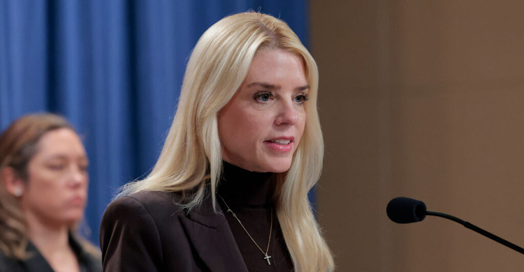 Attorney General Pam Bondi in a brown turtleneck and brown jacket speaking at a podium