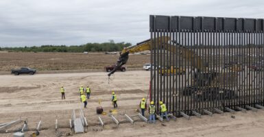 A large excavator begins to dig into the ground near where a wall is being built along the southern border.