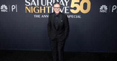 Stephen Colbert stands with his hands in his pockets oni the red carpet.