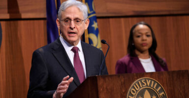 Attorney General Merrick Garland in a black suit and red tie speaks at lectern in Louisville Kentucky
