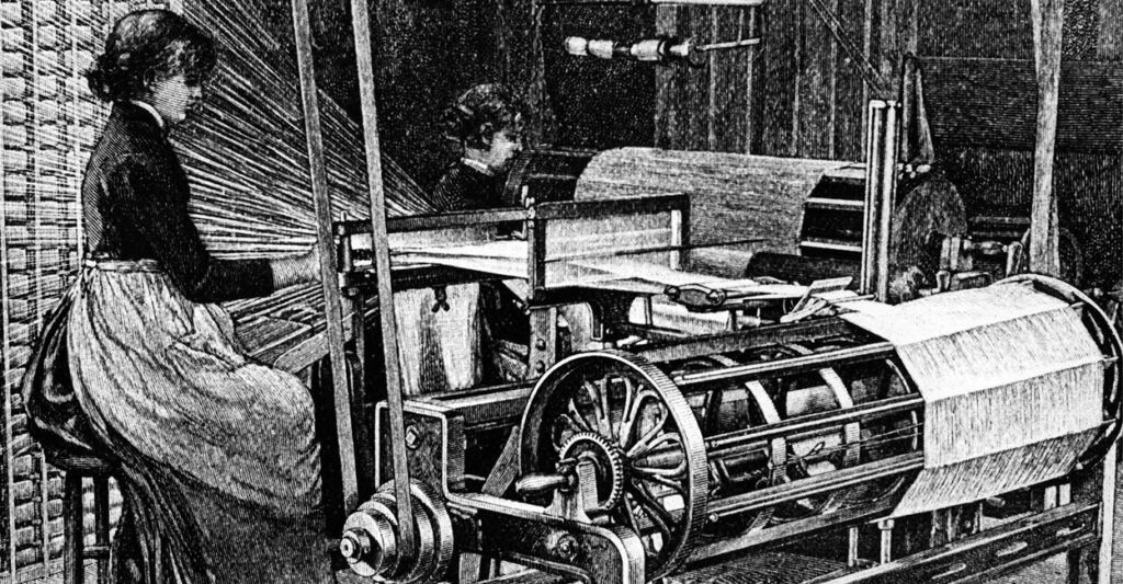 A woman sits in a building in 1885 making the warp threads through the harness to form pattern.
