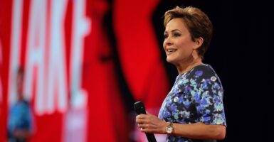 Kari Lake stands and holds a microphone in her left hand and looks out at the audience.