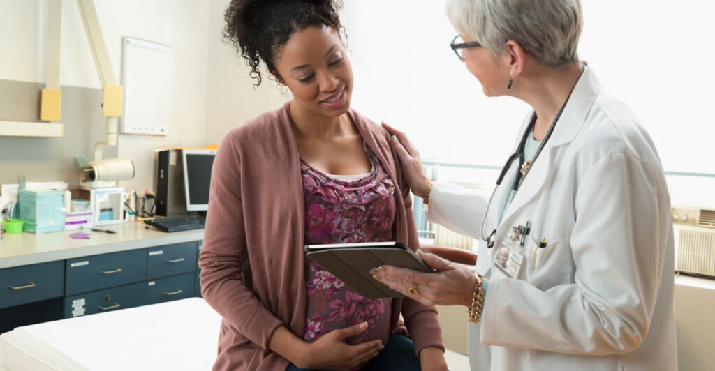 a female doctor showing a pregnant black patient something on her electronic tablet in the doctor's office