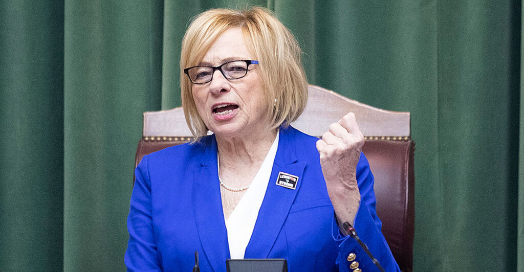 Maine Gov. Janet Mills in a blue suit jacket and glasses holds up her fist while speaking emphatically