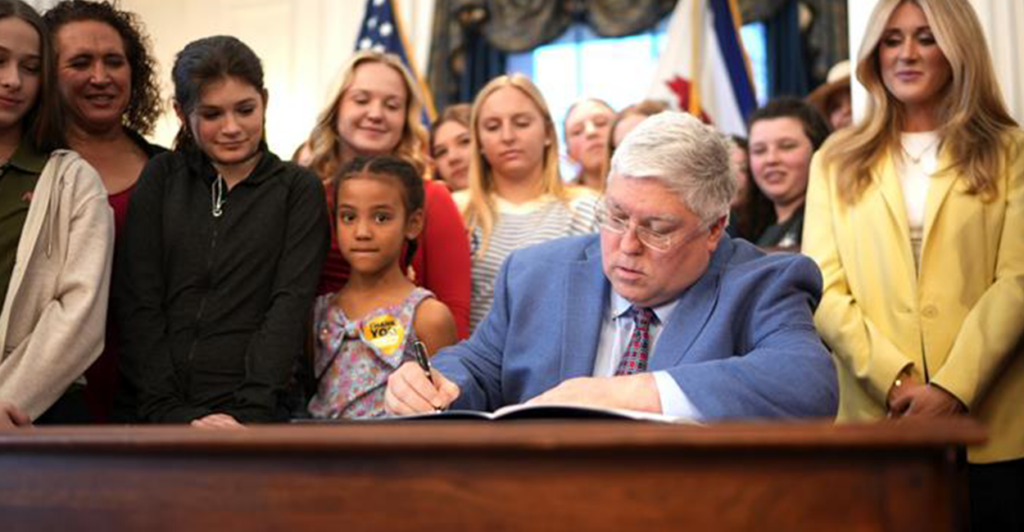 Riley Gaines watches as Gov. Patrick Morrisey of West Virginia signs the Riley Gaines Act into law.