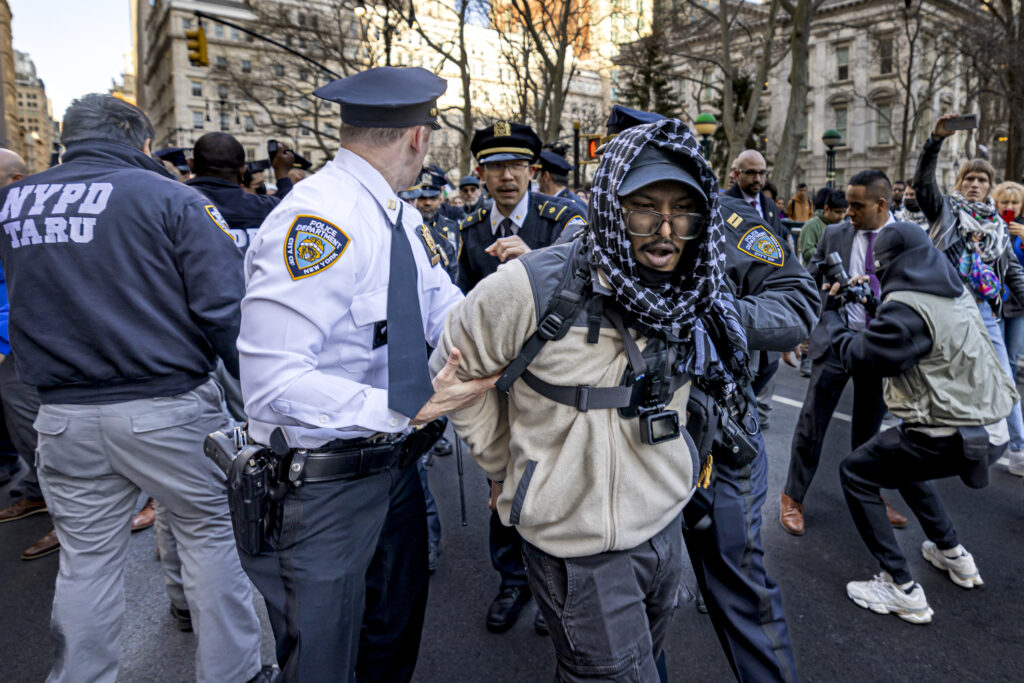 A police officer has his hand on the arm of a man being arrested but is looking behind him.