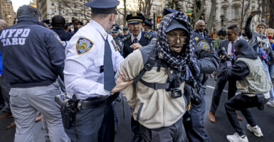 A police officer has his hand on the arm of a man being arrested but is looking behind him.