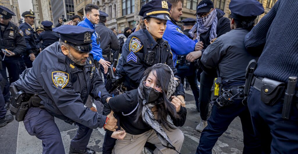 A woman is on her knees as two nearby police officers grab her.