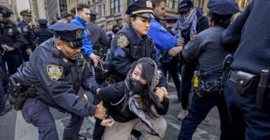 A woman is on her knees as two nearby police officers grab her.