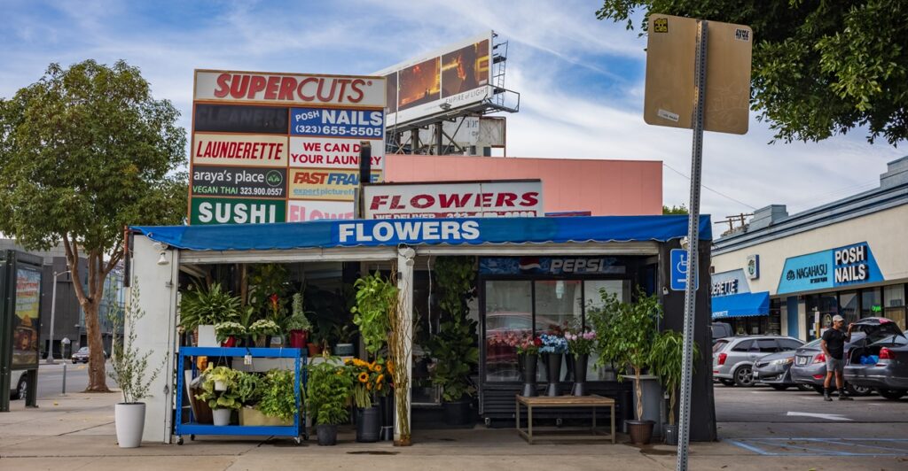 A small open-ended building has a sign that says, "Flowers" while in the background are numerous other business signs.