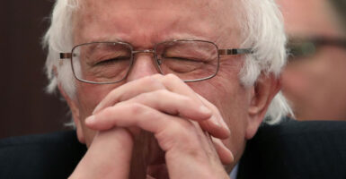 Clos-up of Sen. Bernie Sanders with his face resting on his folded hands with his eyes closed, as if he were praying.