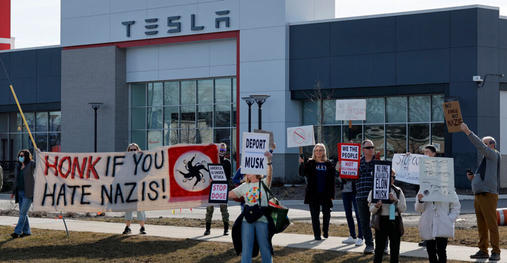 protesters in front of a Tesla dealership holding up signs like honk if you hate Nazis