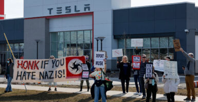 protesters in front of a Tesla dealership holding up signs like honk if you hate Nazis