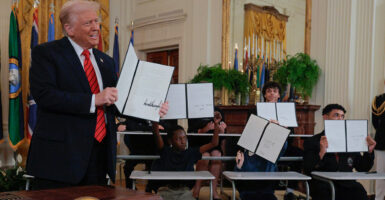 Joined by children seated at school desks at a White House ceremony Thursday, President Donald Trump holds up the signed executive order intended to reduce the size and scope of the federal Education Department.