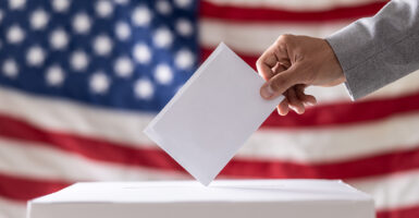 A voter drops his ballot into a ballot box with an American flag unfurled as backdrop.