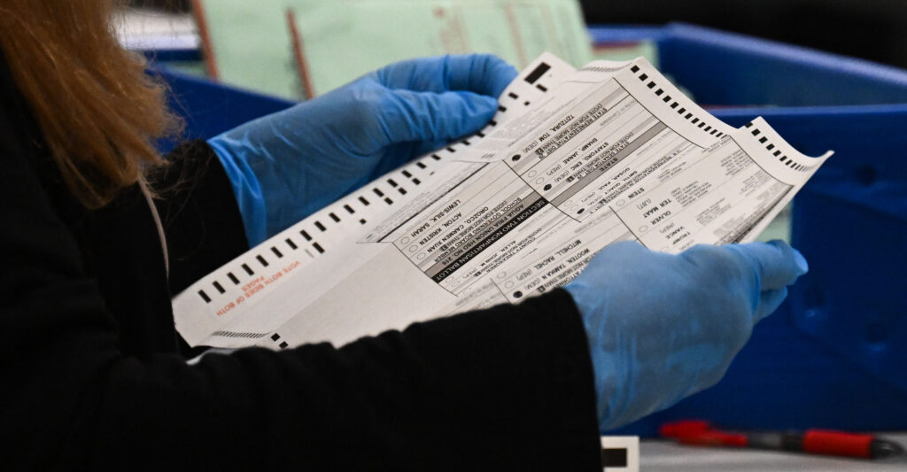 An election worker with latex gloves unfolds a mail-in voter ballot