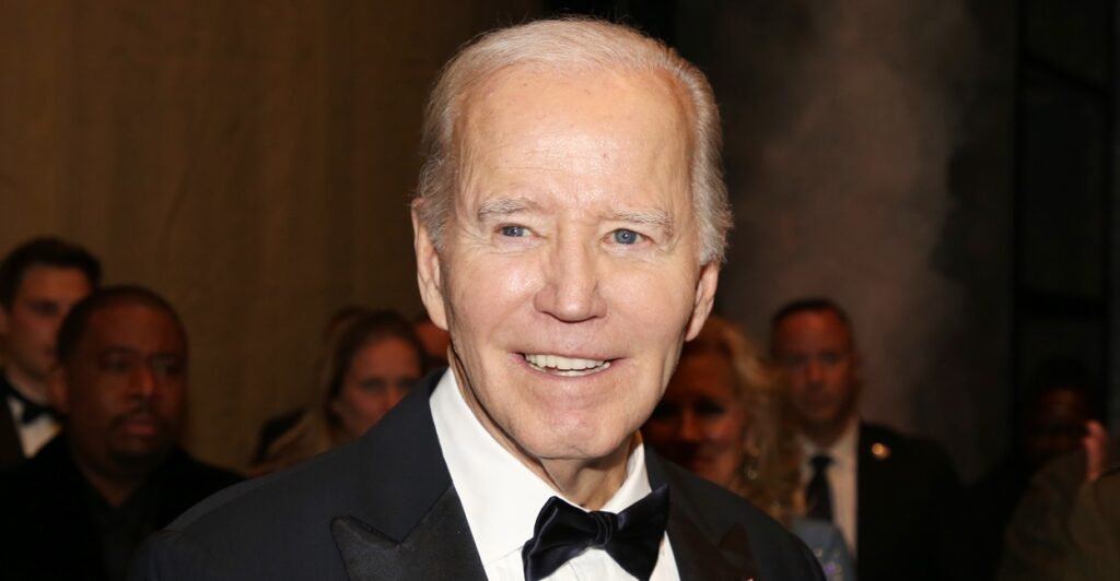 Joe Biden is standing at a reception and smiles with his head turned to his right.