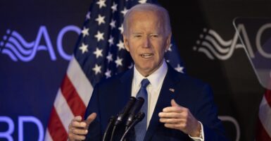 Joe Biden stands in front of a microphone behind a podium as he motions with his hands while talking.