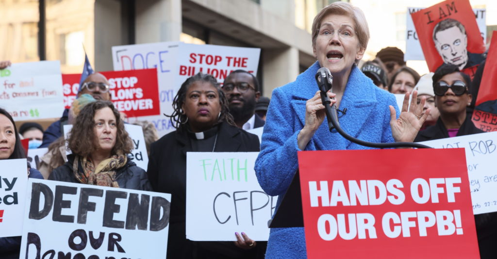 Sen. Elizabeth Warren speaks at an anti-DOGE rally, backed by sign-caring protesters, in defense of the Consumer Finance Protection Bureau.