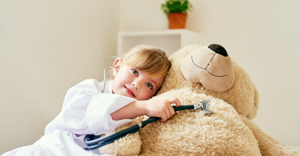 Adorable little girl pretends to be doctor treating her large teddy bear.