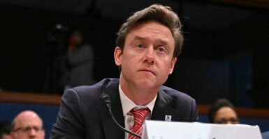 Michael Johnston sits at a desk while testifying with a microphone and name plate in front of him.