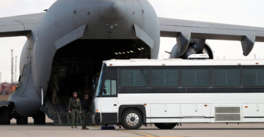 Large white bus parked next to the back of large cargo plane, its cargo door open wide.