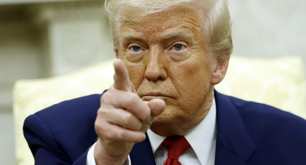 Donald Trump in a blue suit with a red tie points