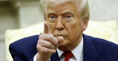 Donald Trump in a blue suit with a red tie points