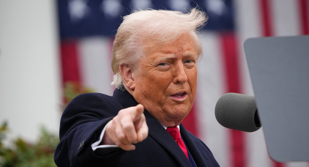 Donald Trump in a black suit points and smiles