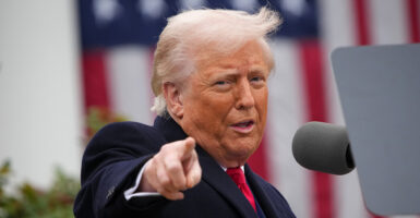 Donald Trump in a black suit points and smiles