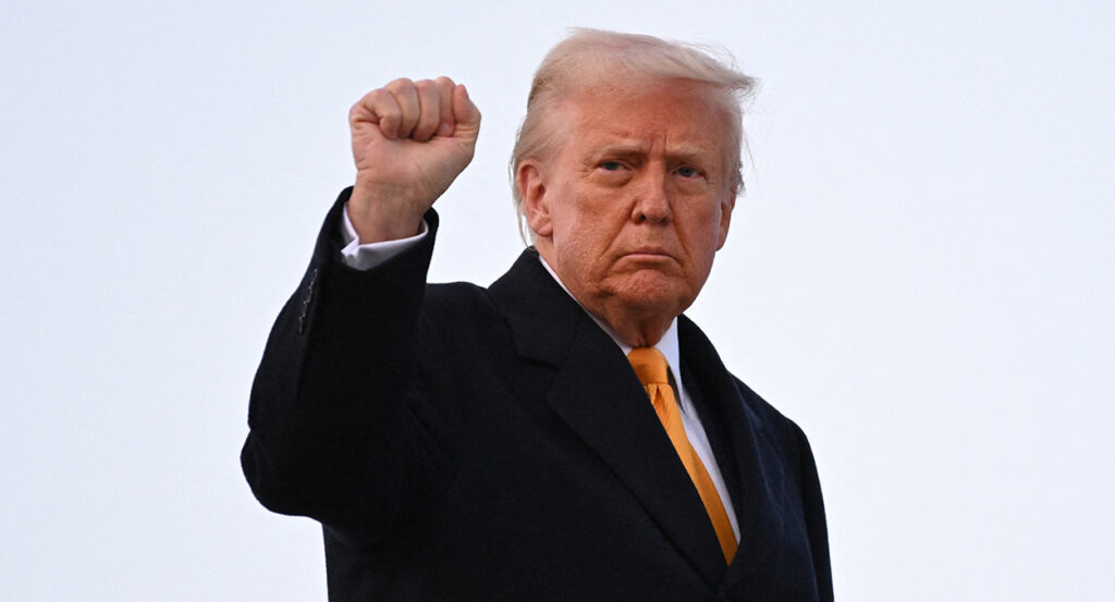Donald Trump in a black coat raises his fist.