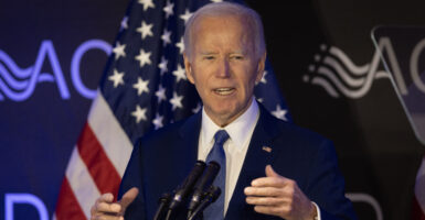 former President Joe Biden in a blue suit and blue tie speaking at a podium with an American flag in the background