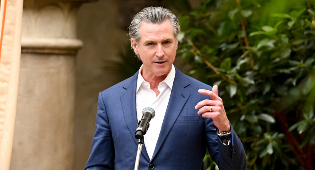 Gavin Newsom gestures while wearing a blue suit