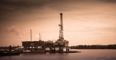A sepia-tone image of an oil rig along the water.
