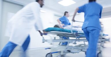 Two nurses in blue and a doctor race a female patient