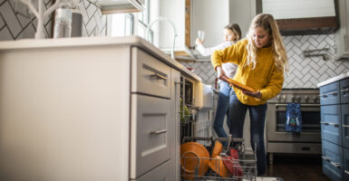 A blonde girl and brunette girl help load dishwasher.
