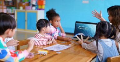 Little children in a classroom listen in rapt attention to their teacher.
